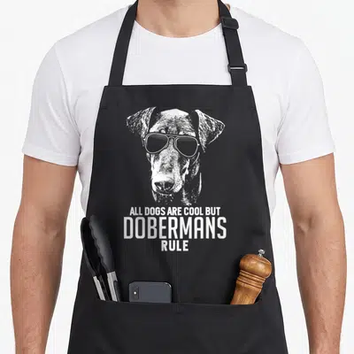 Doberman dog rules apron - White distressed doberman head with sunglasses above stacked text on black apron — shown on a black cotton canvas apron against a white background