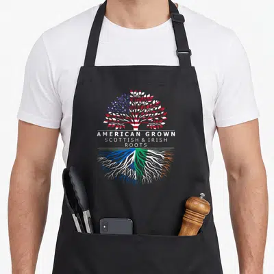Irish american flag apron - Tree with US flag leaves and blue white green orange roots under text — shown on a black cotton canvas apron against a white background