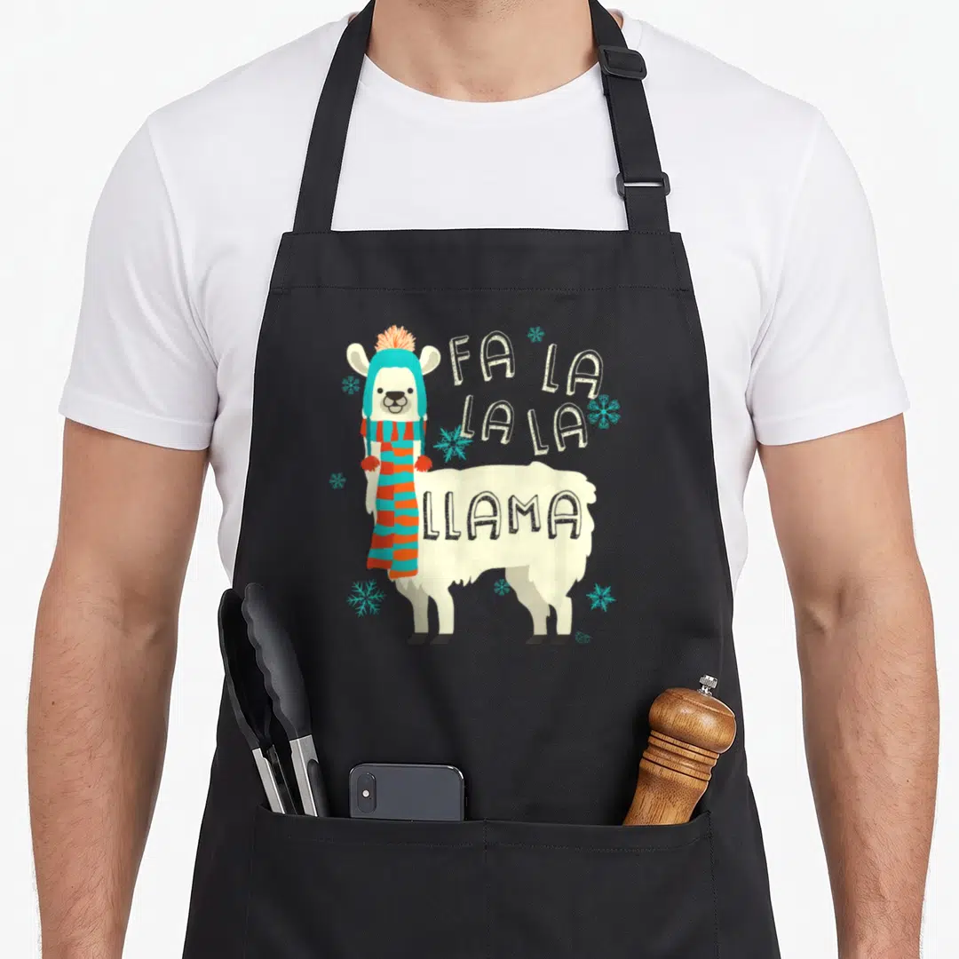 Llama christmas alpaca apron - Cartoon cream llama in blue hat and striped scarf next to Fa La La Llama text and blue — shown on a black cotton canvas apron against a white background