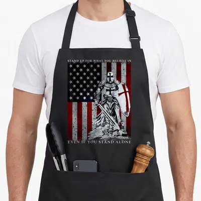 Templar american flag apron - Knight holding sword and cross shield in front of distressed American flag with text — shown on a black cotton canvas apron against a white background