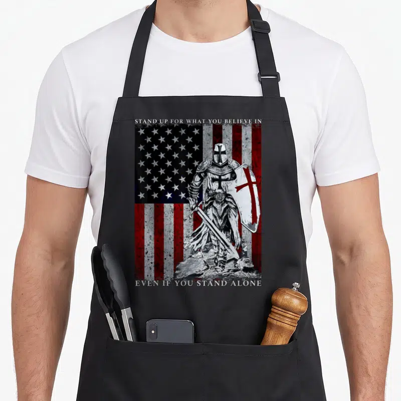 Templar american flag apron - Knight holding sword and cross shield in front of distressed American flag with text — shown on a black cotton canvas apron against a white background