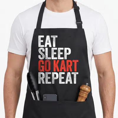 Eat racing apron - Stacked EAT SLEEP GO KART REPEAT text in distressed white and red fonts — shown on a black cotton canvas apron against a white background