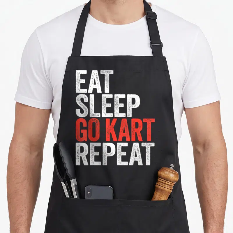 Eat racing apron - Stacked EAT SLEEP GO KART REPEAT text in distressed white and red fonts — shown on a black cotton canvas apron against a white background