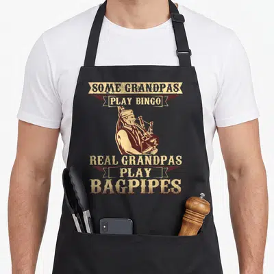 Bagpipe bingo apron - Retro illustration of man playing bagpipes with text banners reading Some Grandpas Play Bingo — shown on a black cotton canvas apron against a white background