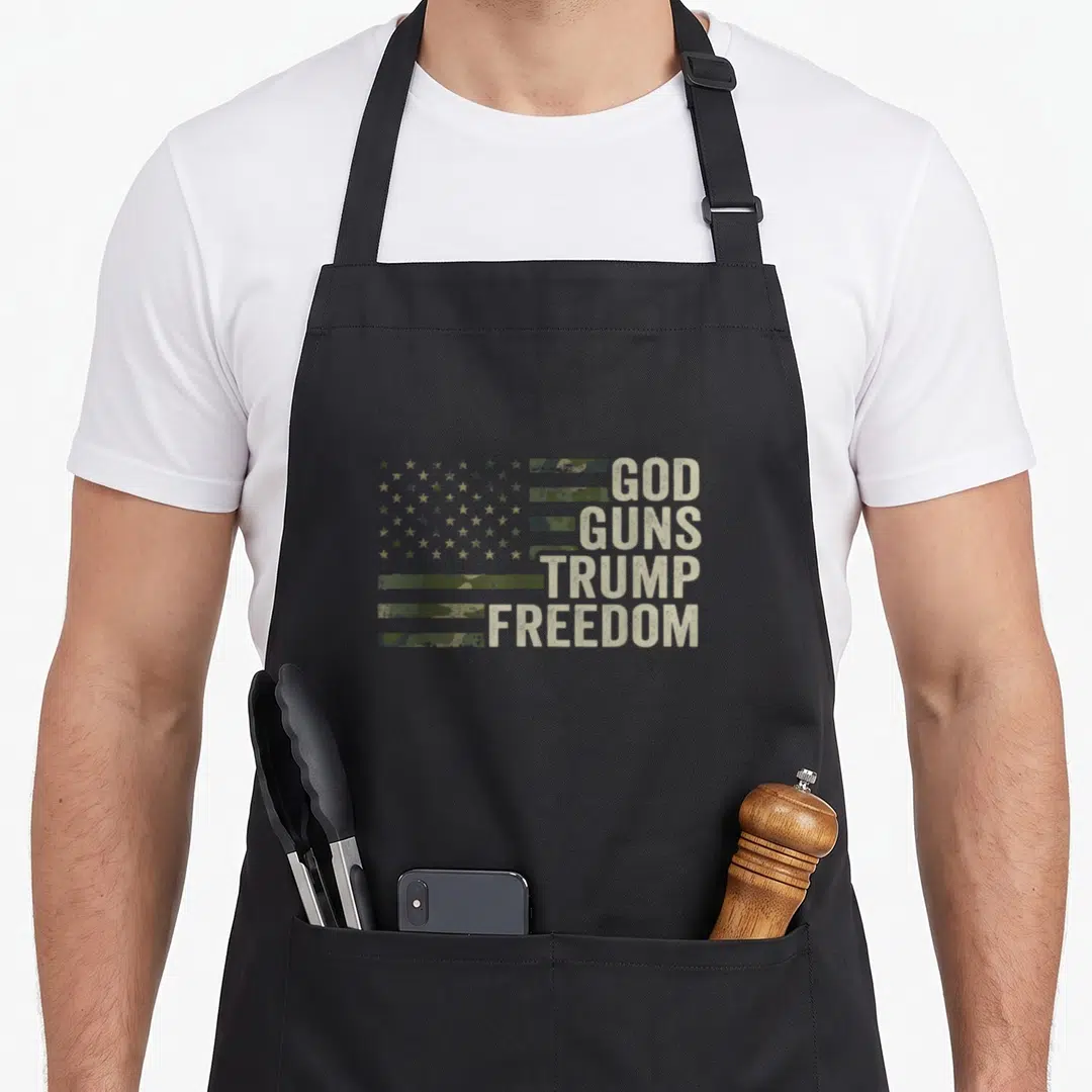 God pro apron - Camo USA flag with tan stars and olive stripes next to stacked distressed text reading God Guns Trump — shown on a black cotton canvas apron against a white background