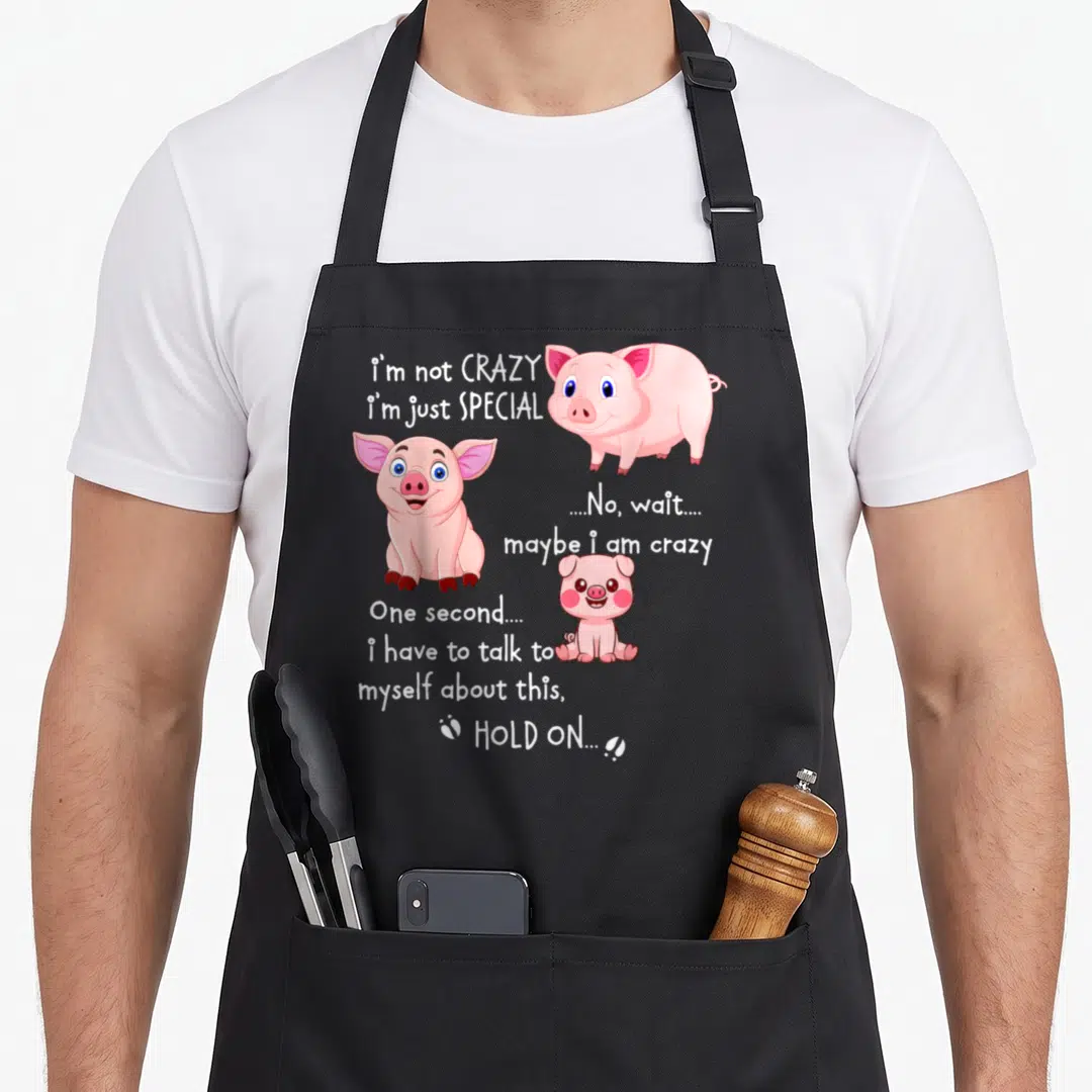 Pig special aprons - Three pink cartoon pigs with white text reading I'm not crazy I'm just special — shown on a black cotton canvas apron against a white background