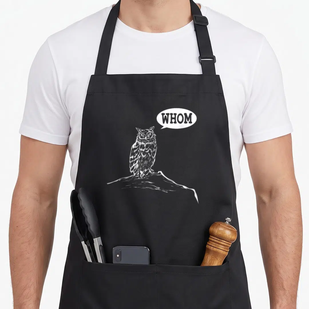 Whom teacher apron - White owl on rock with speech bubble reading WHOM in line art style — shown on a black cotton canvas apron against a white background