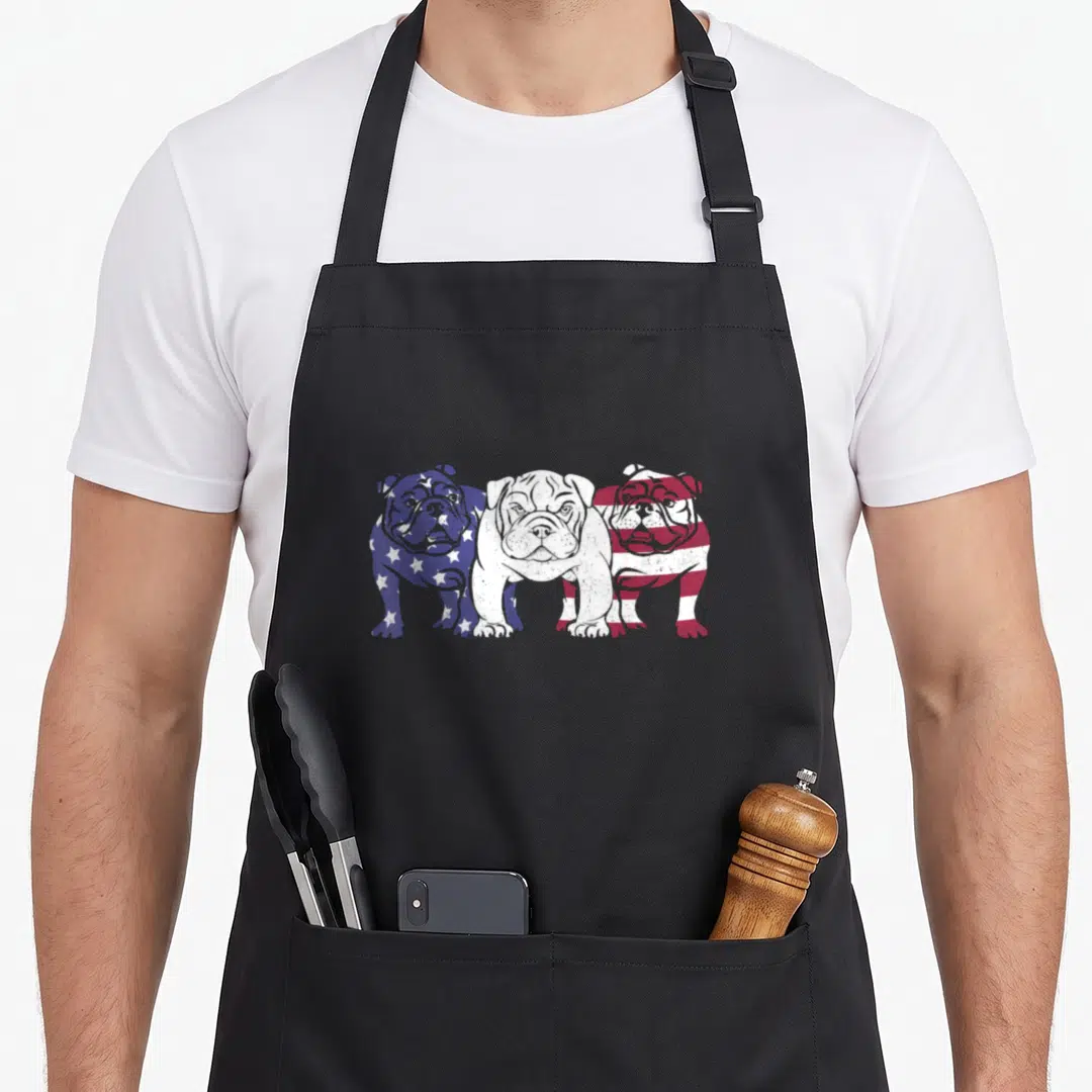 Unique american flag apron - Three bulldogs standing side-by-side colored in blue stars and red stripes — shown on a black cotton canvas apron against a white background