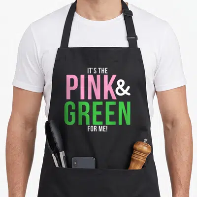 Funny sorority apron - Stacked pink green and white text reading IT'S THE PINK & GREEN FOR ME! — shown on a black cotton canvas apron against a white background
