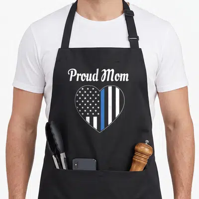 Law police apron - Proud Mom text above heart with thin blue line flag pattern in grey white and blue — shown on a black cotton canvas apron against a white background