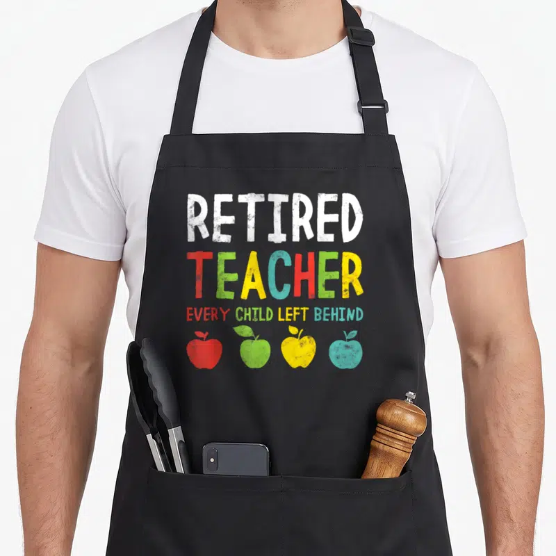 Left teachers apron - Distressed text reading Retired Teacher Every Child Left Behind above four red, green, yellow — shown on a black cotton canvas apron against a white background