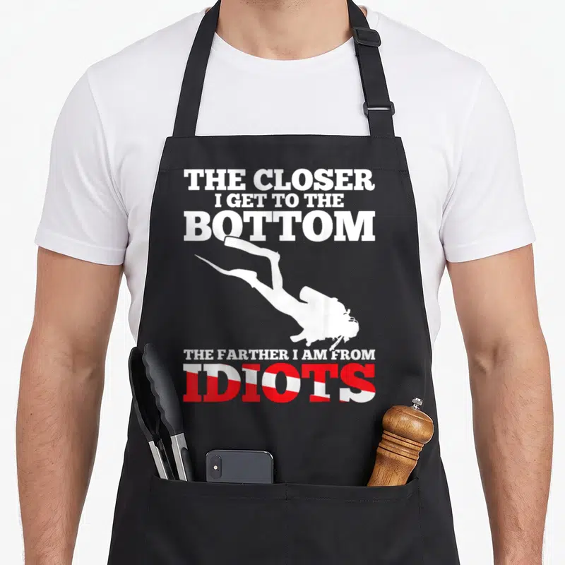 Flag dive diving apron - Scuba diver silhouette between text with red and white striped IDIOTS letters — shown on a black cotton canvas apron against a white background