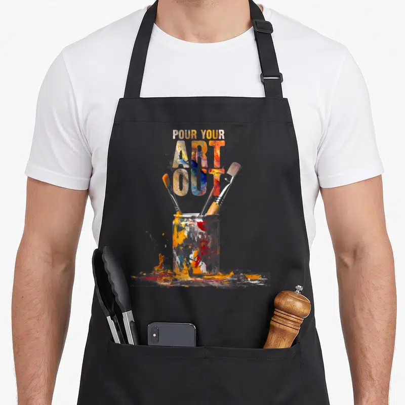 Cat painter apron - Stacked text over paint jar with three brushes and orange blue red yellow white splashes — shown on a black cotton canvas apron against a white background