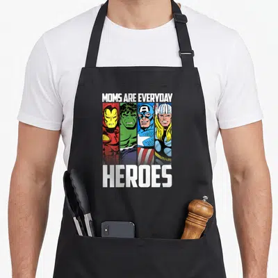 Heroe mother's day aprons - MOMS ARE EVERYDAY HEROES text above and below four superhero faces in red, green, blue — shown on a black cotton canvas apron against a white background