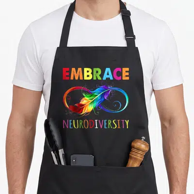 Embrace rainbow apron - Rainbow EMBRACE NEURODIVERSITY text with infinity symbol and feather illustration — shown on a black cotton canvas apron against a white background