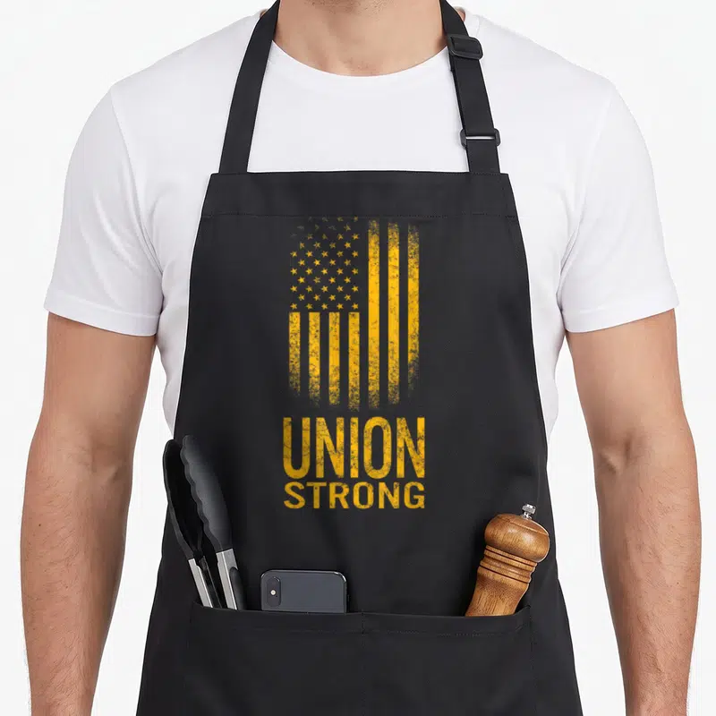 Fist union aprons - Distressed yellow flag above stacked UNION STRONG text in vintage style — shown on a black cotton canvas apron against a white background