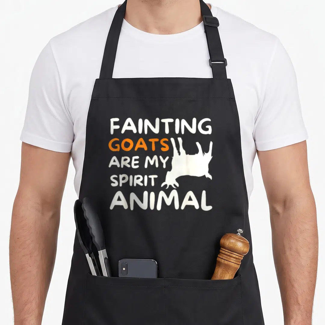 Fainting goat apron - Stacked text reading FAINTING GOATS ARE MY SPIRIT ANIMAL with a white goat silhouette — shown on a black cotton canvas apron against a white background