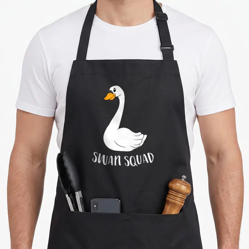 Squad swan lover apron - Cartoon white swan with orange beak above SWAN SQUAD text — shown on a black cotton canvas apron against a white background