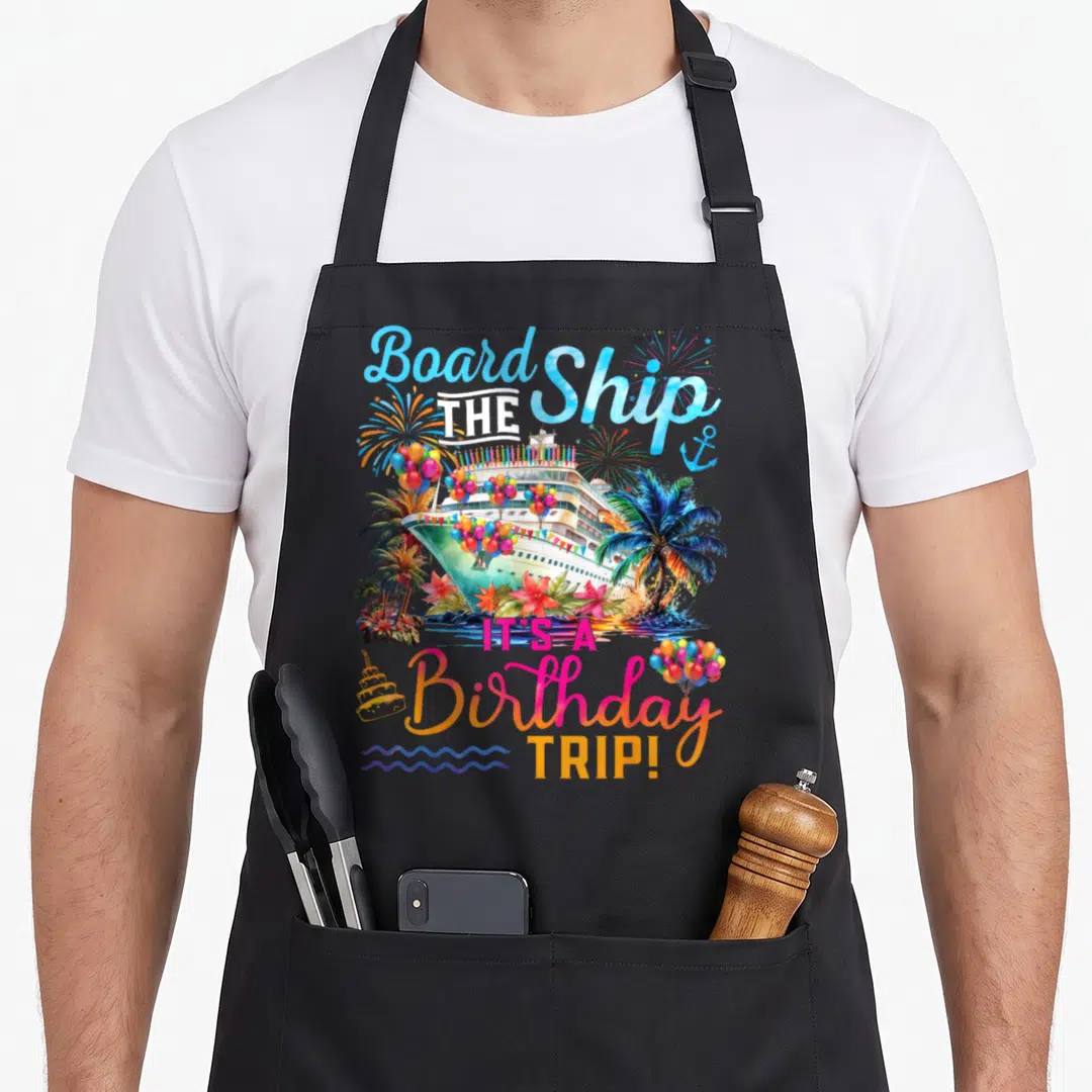 Board birthday apron - Watercolor cruise ship with balloons, palm trees, and text reading Board The Ship It's — shown on a black cotton canvas apron against a white background