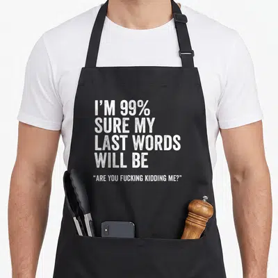 Humorous joke apron - White distressed text reading I'm 99% Sure My Last Words Will Be Are You Kidding Me — shown on a black cotton canvas apron against a white background