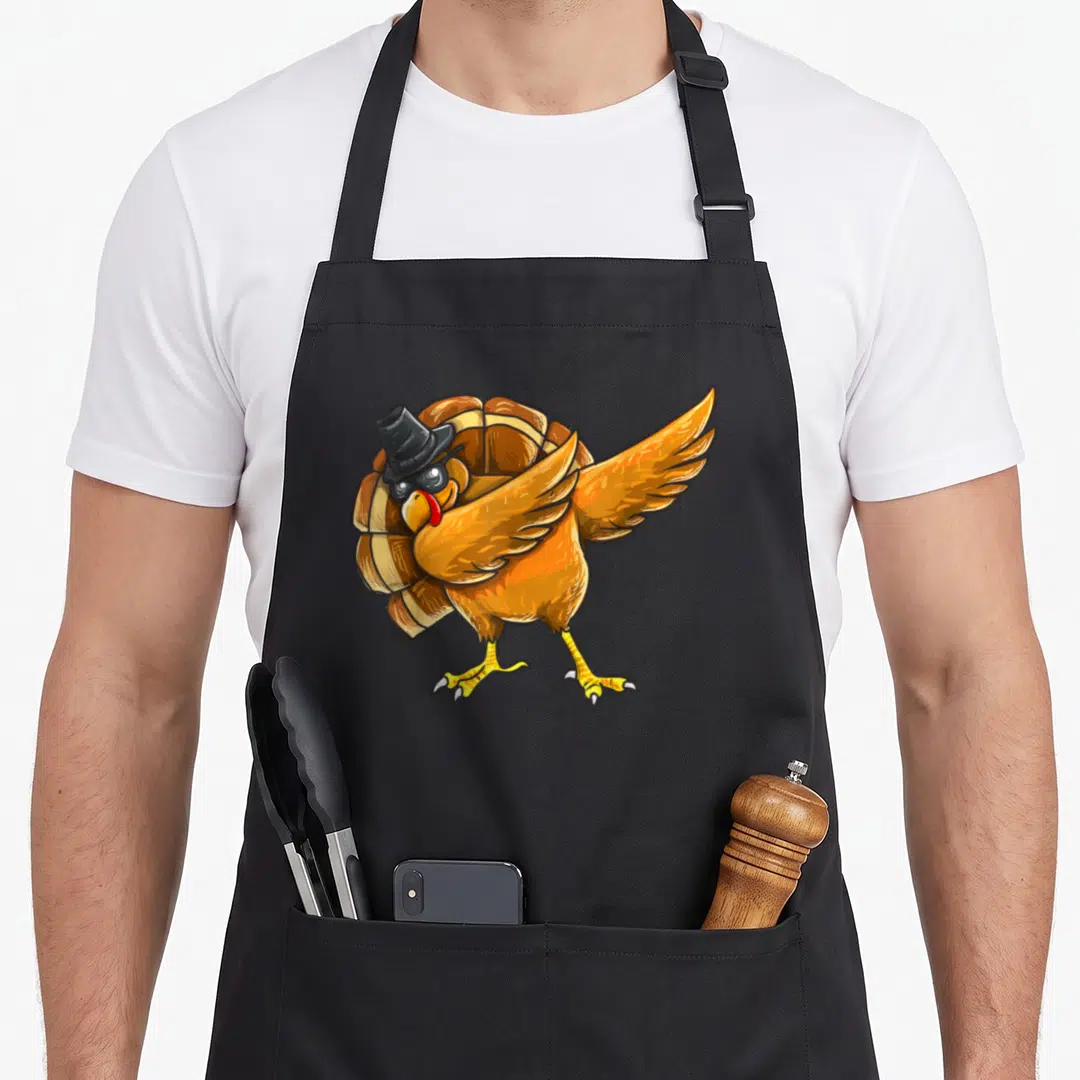 Dabbing thanksgiving day aprons - Cartoon turkey in black hat and sunglasses doing a dab pose in orange and yellow — shown on a black cotton canvas apron against a white background