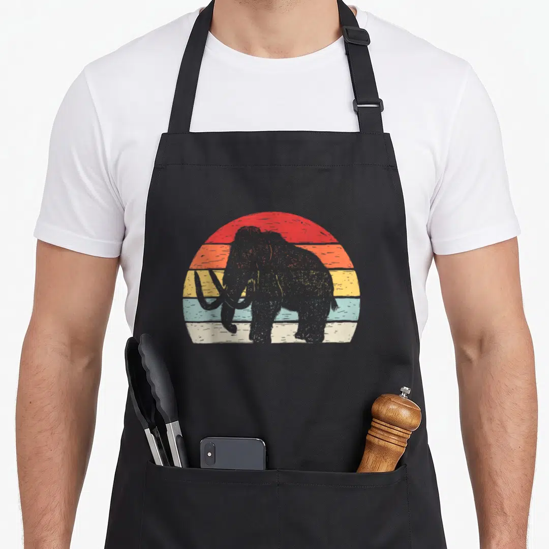 Catch animal print apron - Grey woolly mammoth silhouette against a retro sun with red orange yellow blue and white — shown on a black cotton canvas apron against a white background