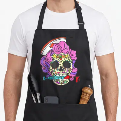 Sugar nursing student apron - Cartoon sugar skull with nurse hat, pink hair, syringe in teeth, colorful dots in pink — shown on a black cotton canvas apron against a white background