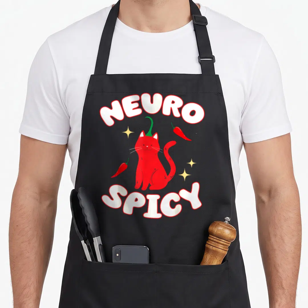 Neurospicy cat apron - Red cartoon cat with chili pepper tail between arched NEURO SPICY text and yellow sparkles — shown on a black cotton canvas apron against a white background