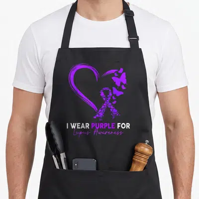 Lupus heart family apron - Purple heart outline containing ribbon made of small hearts and butterflies with awareness — shown on a black cotton canvas apron against a white background