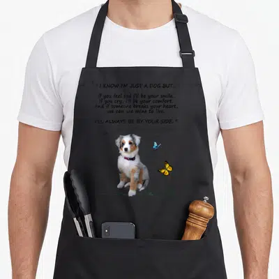 Ill australian apron - Sitting Australian Shepherd puppy with quote text, blue and yellow butterflies, and green grass — shown on a black cotton canvas apron against a white background