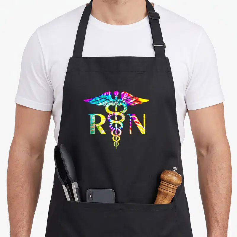 Lovely tie dye apron - RN letters and caduceus filled with blue yellow red green purple tie-dye pattern — shown on a black cotton canvas apron against a white background