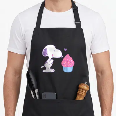Valentine cupcake apron - Snoopy beside pink cupcake with purple heart and blue wrapper — shown on a black cotton canvas apron against a white background