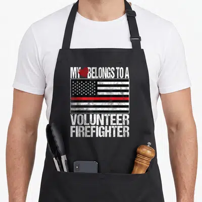 Line firefighter apron - Distressed flag with red stripe and My Heart Belongs To A Volunteer Firefighter text — shown on a black cotton canvas apron against a white background