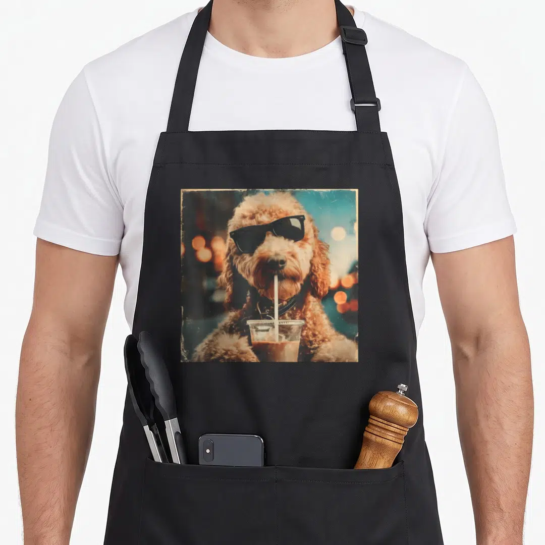 Goldendoodle drinking dog apron - Brown dog in black sunglasses drinking iced coffee with a straw against a teal — shown on a black cotton canvas apron against a white background