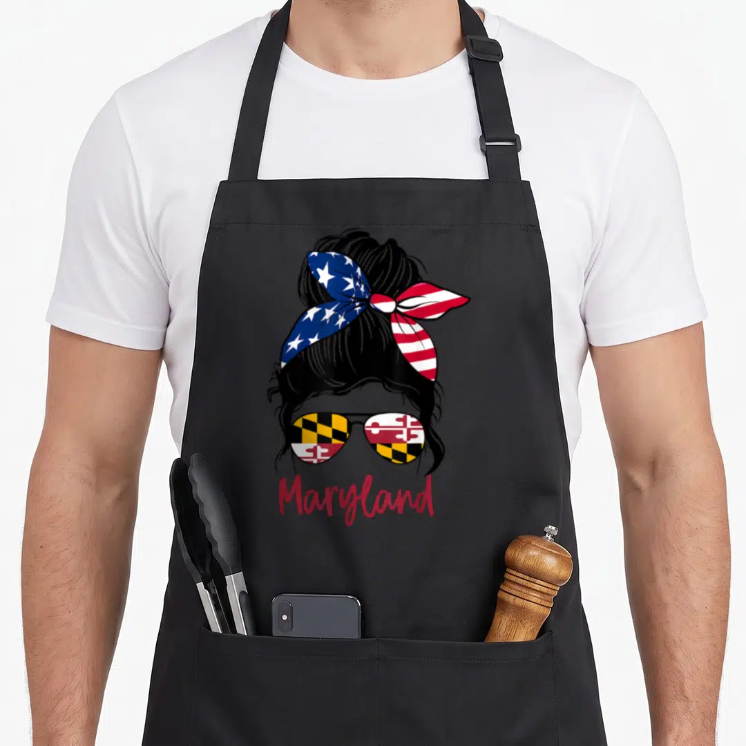 Maryland messy aprons - Cartoon woman with bun, US bandana, Maryland flag sunglasses, red Maryland text — shown on a black cotton canvas apron against a white background