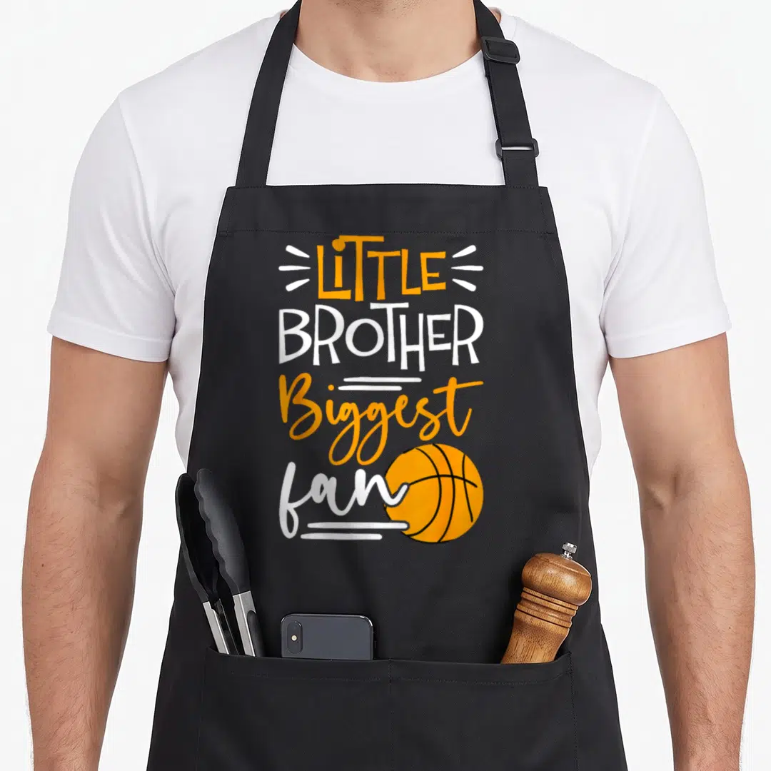 Brother basketball boys apron - Vertical LITTLE BROTHER Biggest fan text with orange basketball and white lines — shown on a black cotton canvas apron against a white background