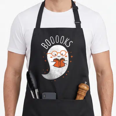 Booook halloween apron - White ghost wearing orange glasses holding an orange book under arched text BOOOOKS — shown on a black cotton canvas apron against a white background