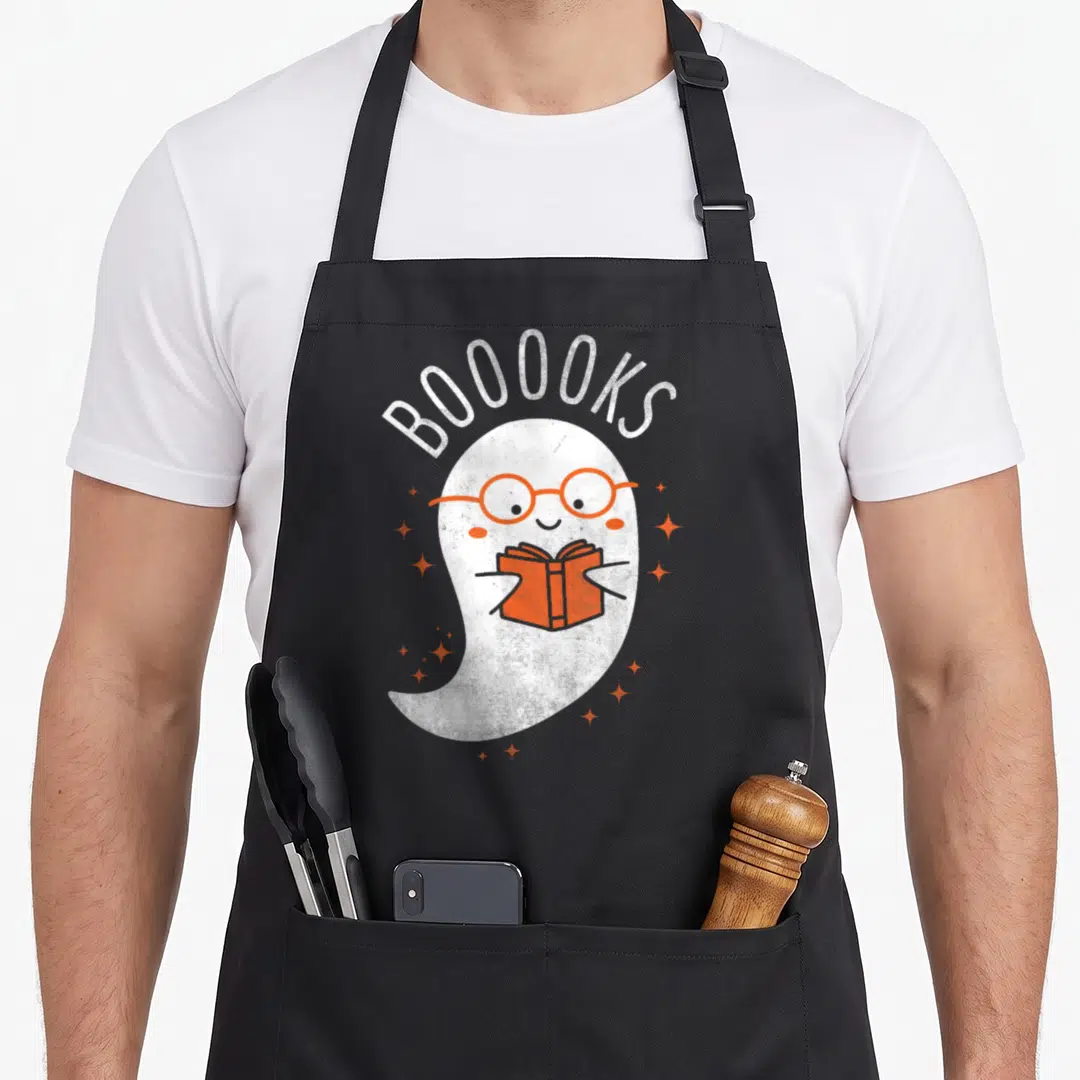 Booook halloween apron - White ghost wearing orange glasses holding an orange book under arched text BOOOOKS — shown on a black cotton canvas apron against a white background