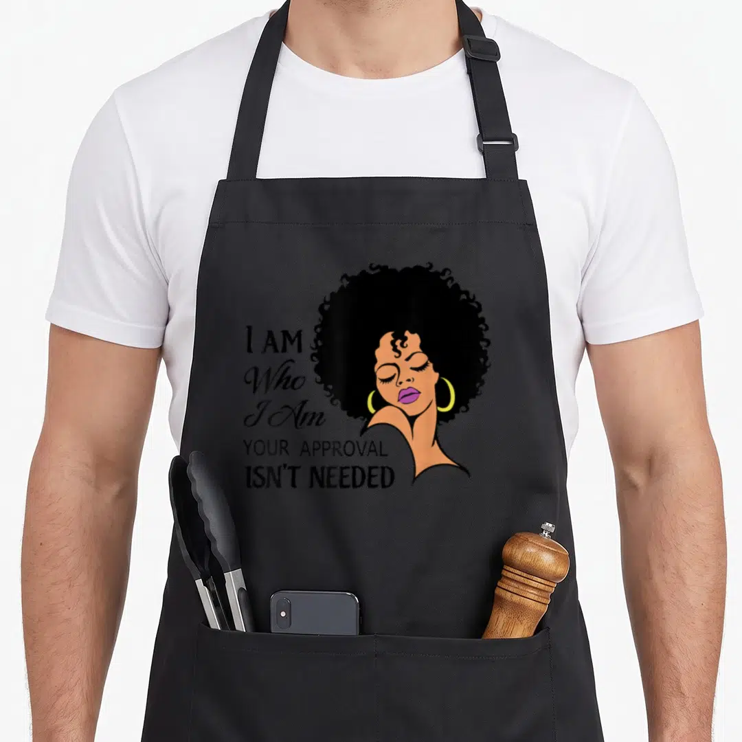 Queen african american aprons - Cartoon woman with afro and text I AM Who I Am YOUR APPROVAL ISN'T NEEDED — shown on a black cotton canvas apron against a white background