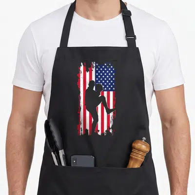 Pitcher american flag apron - Grey baseball pitcher silhouette over distressed red white blue flag — shown on a black cotton canvas apron against a white background