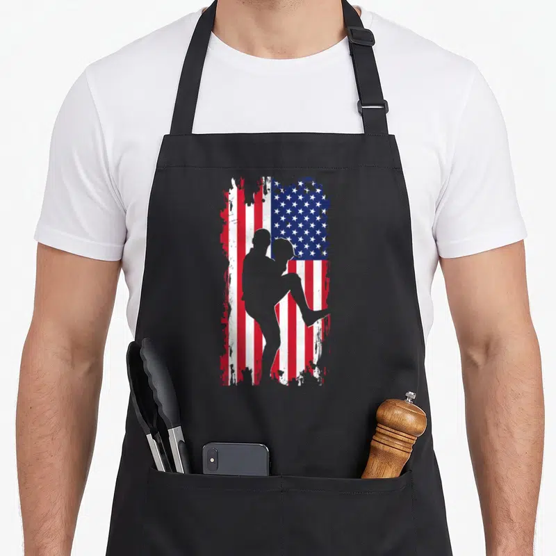 Pitcher american flag apron - Grey baseball pitcher silhouette over distressed red white blue flag — shown on a black cotton canvas apron against a white background