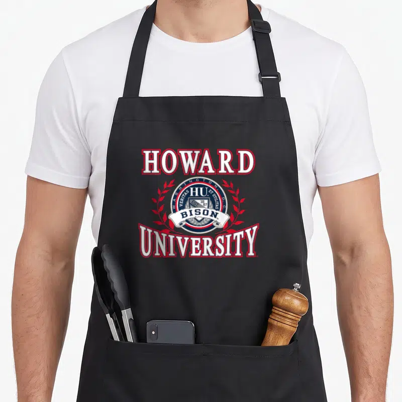 Howard bison man apron - Howard University seal with shield, red laurels, and Bison banner in red white blue — shown on a black cotton canvas apron against a white background