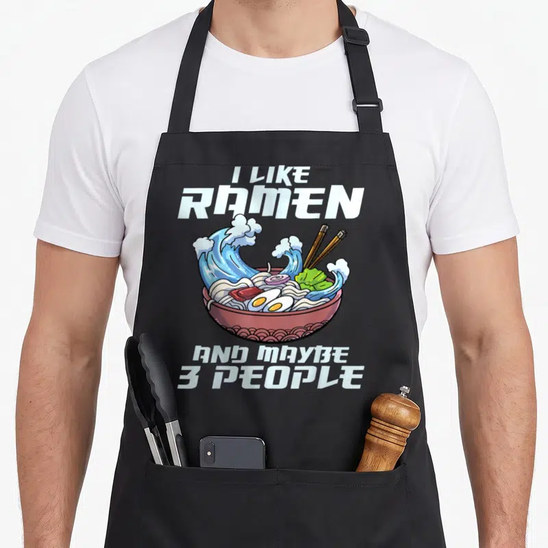 Japanese noodle anime apron - Cartoon ramen bowl with blue waves and text I like ramen and maybe 3 people — shown on a black cotton canvas apron against a white background