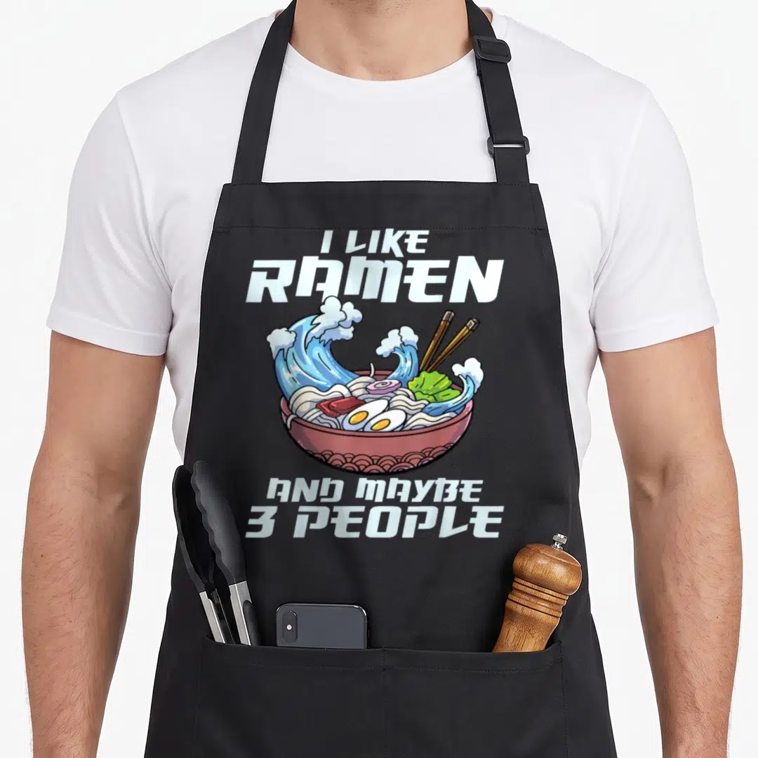 Japanese noodle anime apron - Cartoon ramen bowl with blue waves and text I like ramen and maybe 3 people — shown on a black cotton canvas apron against a white background
