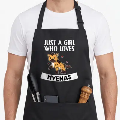 Hyenas hyena apron - Cartoon hyena with hearts and text Just A Girl Who Loves Hyenas — shown on a black cotton canvas apron against a white background