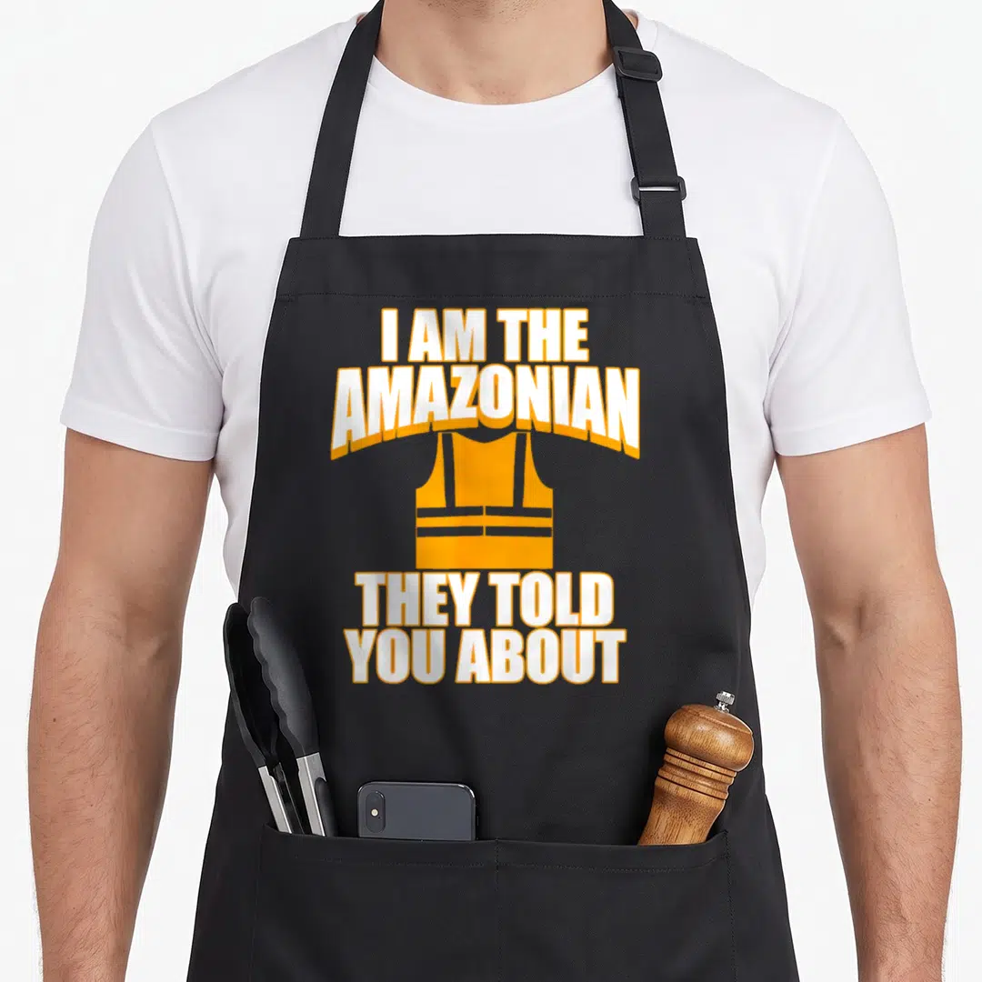 Amazonian swagazon apron - Orange vest graphic between white text reading I AM THE AMAZONIAN THEY TOLD YOU ABOUT — shown on a black cotton canvas apron against a white background