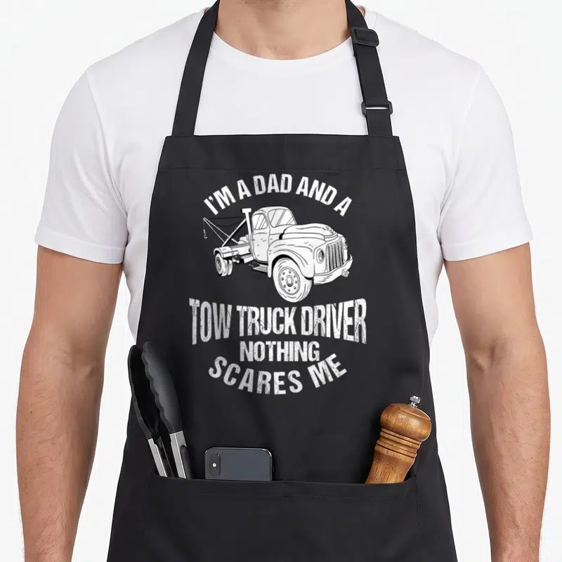 Recovery father day apron - White distressed tow truck illustration with stacked bold text reading I'M A DAD AND A TOW — shown on a black cotton canvas apron against a white background