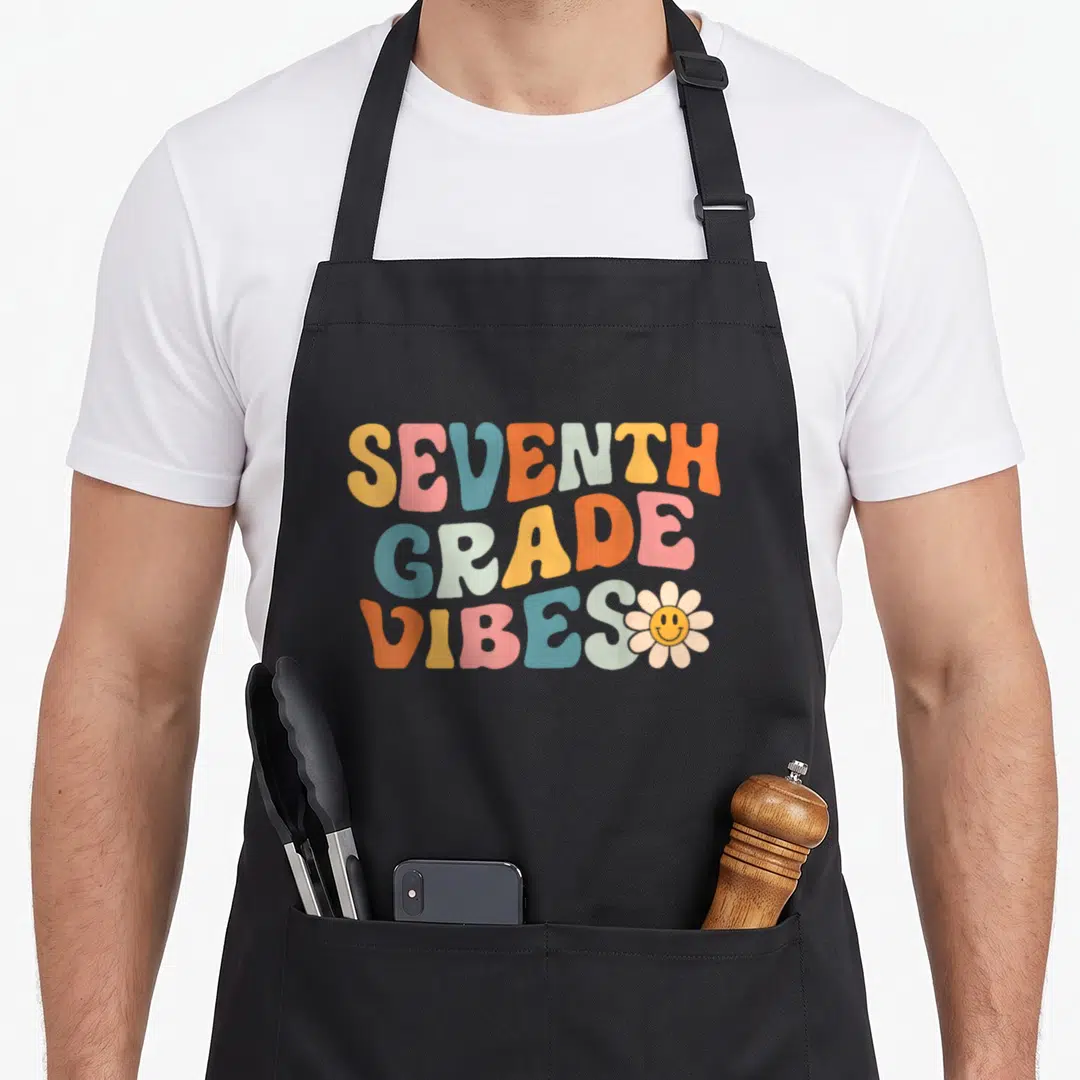 Seventh grade vibes apron - Retro text SEVENTH GRADE VIBES in orange pink blue beige with smiling flower — shown on a black cotton canvas apron against a white background