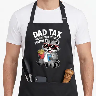 Humorous joke father day apron - Cartoon raccoon with red sunglasses holding fries and blue drink under arched white — shown on a black cotton canvas apron against a white background