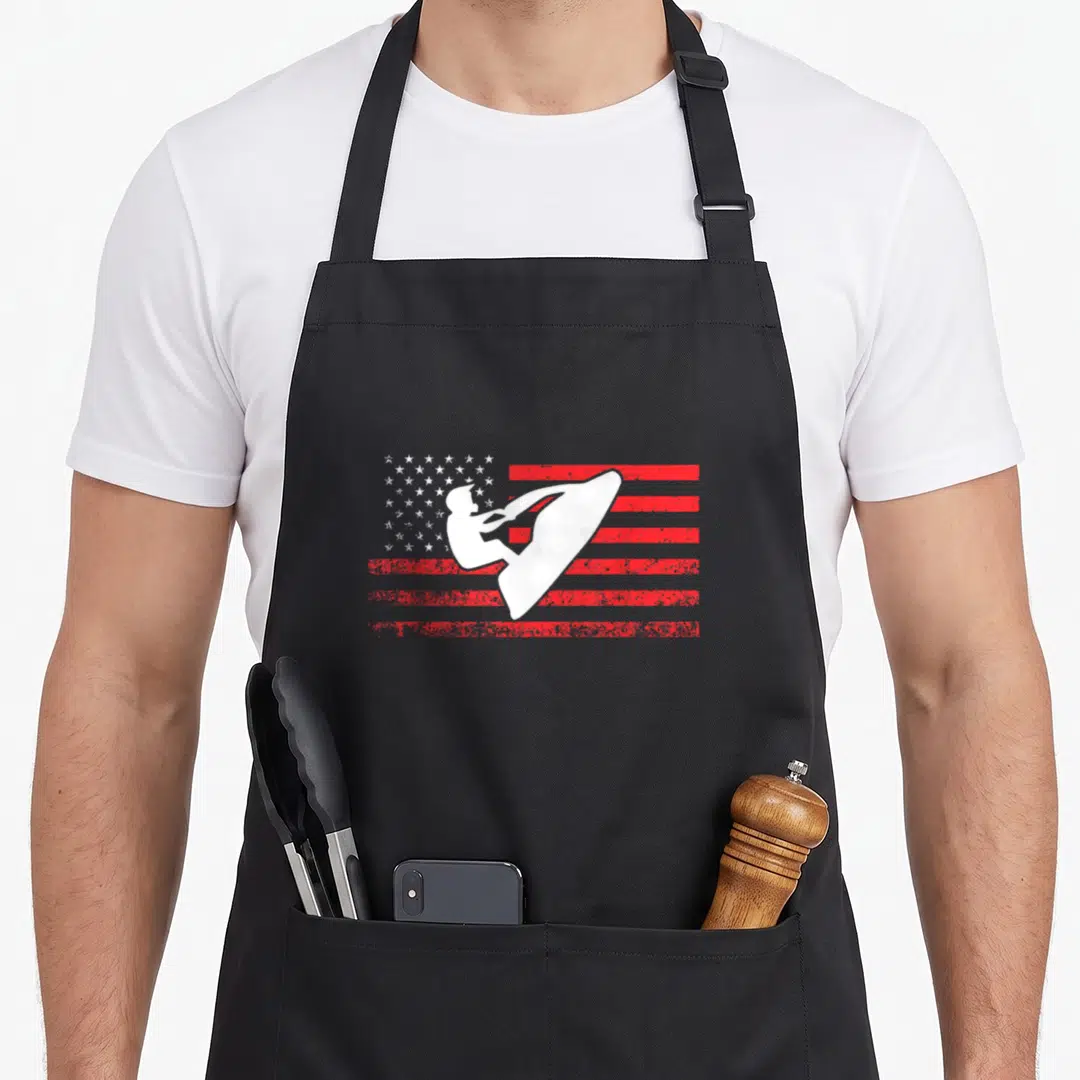 Ski american flag apron - White surfer silhouette on distressed red and white American flag pattern — shown on a black cotton canvas apron against a white background